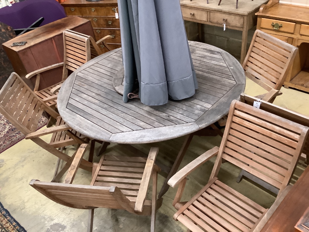 A circular teak garden table, 150cm diameter, height 74cm eight teak folding chairs, parasol and base (parasol rope is broken)